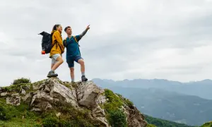 Zwei Wanderer auf einem Felsvorsprung genießen die Aussicht während ihrer Alpen Tour.