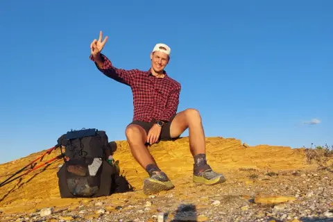 Glücklicher Wanderer mit Rucksack und Stöcken auf einer felsigen Anhöhe, genießt die Aussicht nach einer Etappe des Fischerpfads in Portugal.