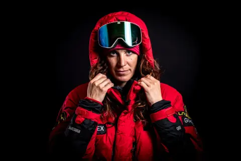 Tamara Lunger, bereit für extreme Bedingungen, zieht ihre rote Kapuze hoch. Ihre Skibrille spiegelt das Licht.