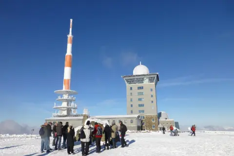 Menschen stehen im Schnee vor dem Brocken-Wetterturm und dem Fernsehturm. Ein sonniger Tag im Winter auf dem Brocken.