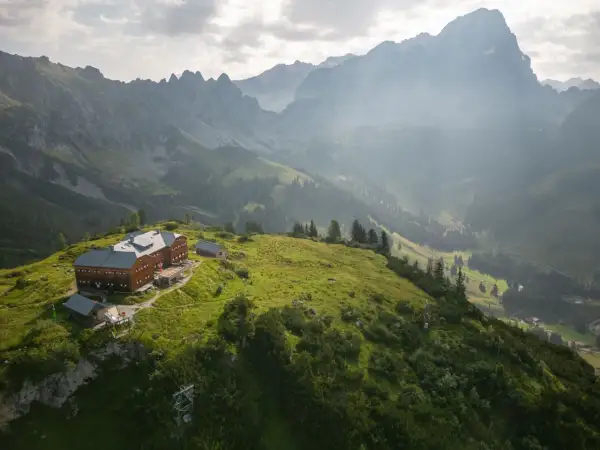 Holzhaus auf einem grünen Hügel, umgeben von majestätischen Bergen. Ein perfekter Ort für die Dachstein Sonnenrunde.