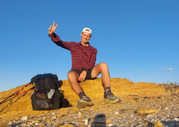 Glücklicher Wanderer mit Rucksack und Stöcken auf einer felsigen Anhöhe, genießt die Aussicht nach einer Etappe des Fischerpfads in Portugal.