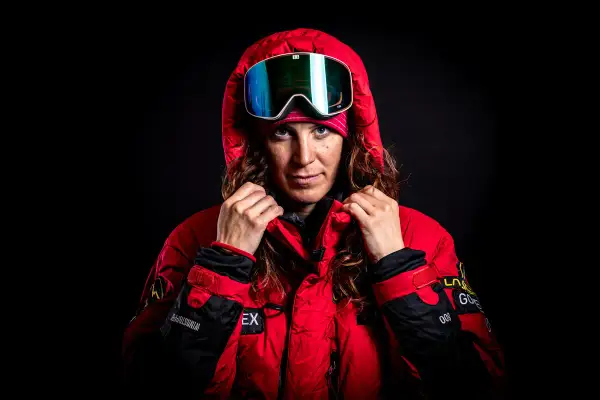 Tamara Lunger, bereit für extreme Bedingungen, zieht ihre rote Kapuze hoch. Ihre Skibrille spiegelt das Licht.