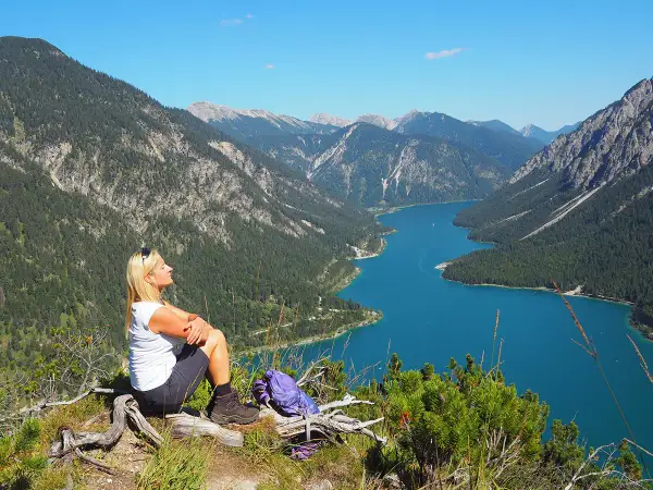 Frau genießt Ausblick beim Plansee Wandern. Türkiser See, grüne Berge und blauer Himmel.